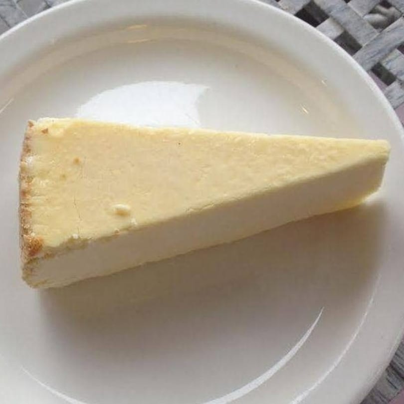 A slice of classic New York cheesecake with a graham cracker crust on a white plate.
